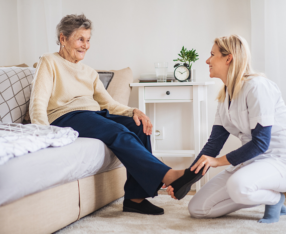 health-visitor-putting-slippers-senior-woman-home-christmas-time 1